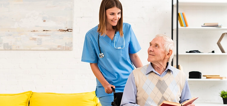 An elderly guy in a wheelchair conversing merrily with a care worker.