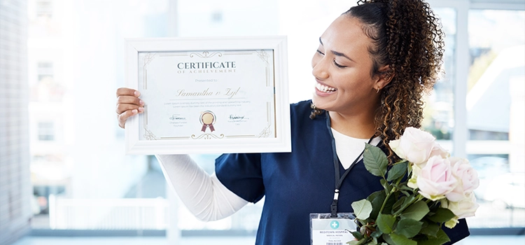 Medical professional proudly displaying her Care Certificate while holding a bouquet of flowers and smiling.