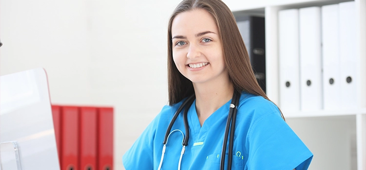 Close-up of woman doctor sitting in office at table, looking at camera and smiling.